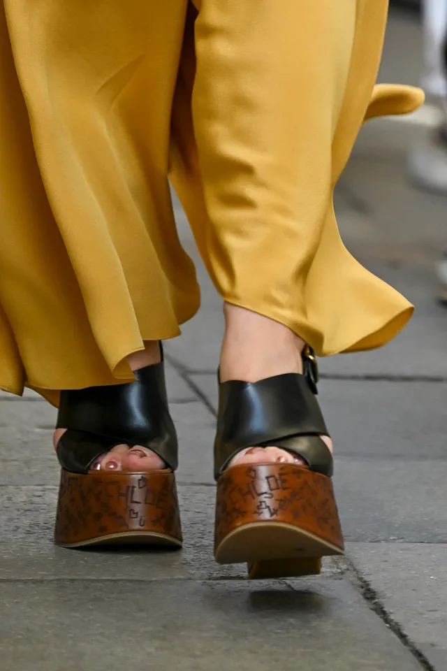 Florence Pugh wearing black platform heels beneath yellow trousers.