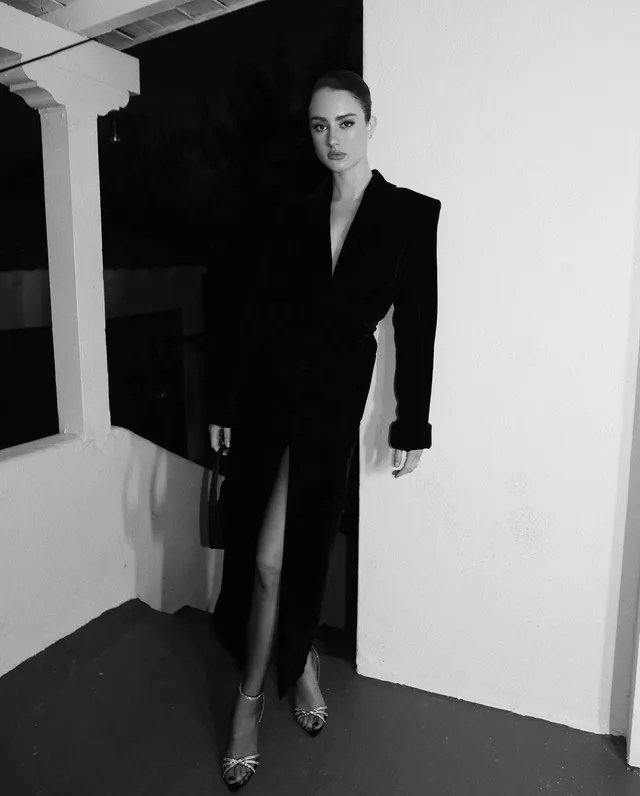 Grace Van Patten posing in a long black coat and open-toe heels.