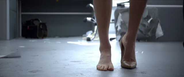 Samara Weaving walking barefoot on an indoor floor in a film scene.