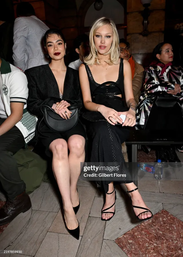 Grace VanderWaal sitting at an event in a black dress and heels.