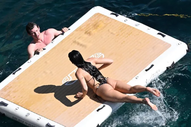 Dua Lipa climbing onto a floating platform beside the sea.