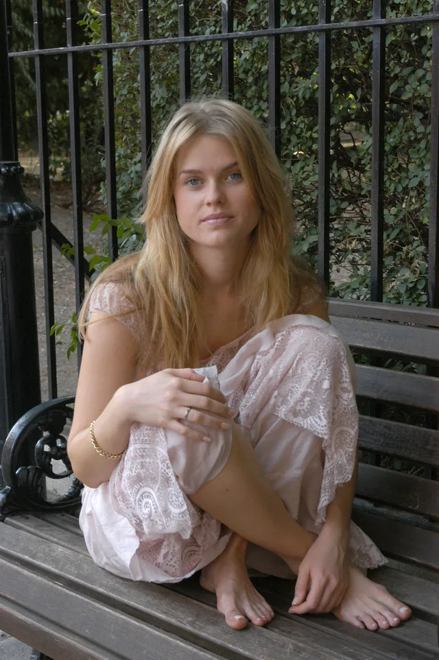 Alice Eve sitting on an outdoor bench in a pale outfit.