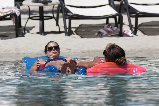 Alex Morgan relaxing barefoot on a pool float beside a companion.