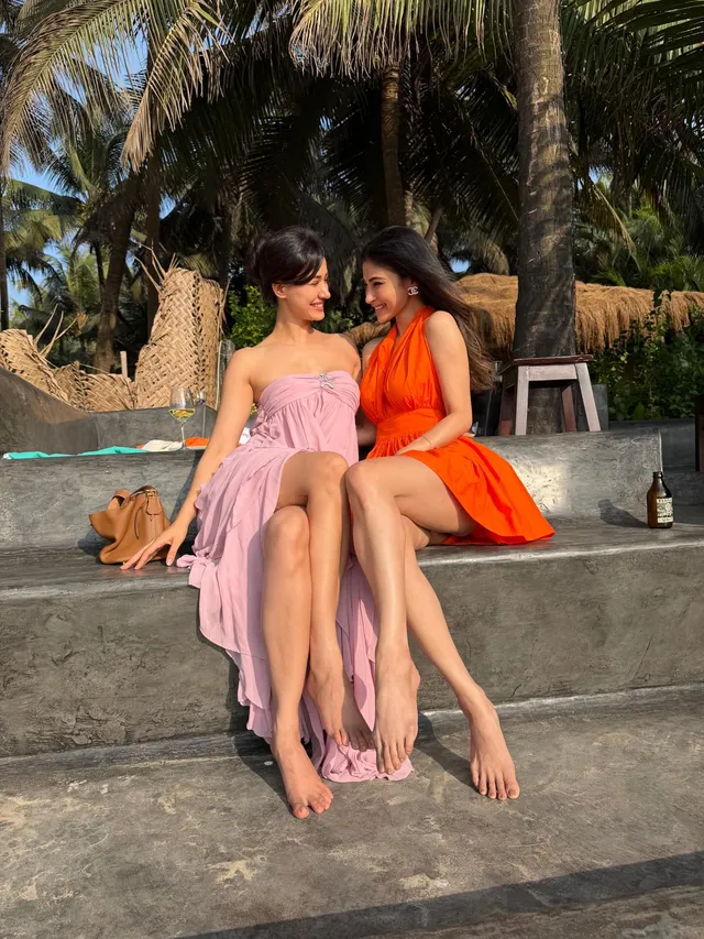 Disha Patani sitting barefoot with a companion on outdoor steps.