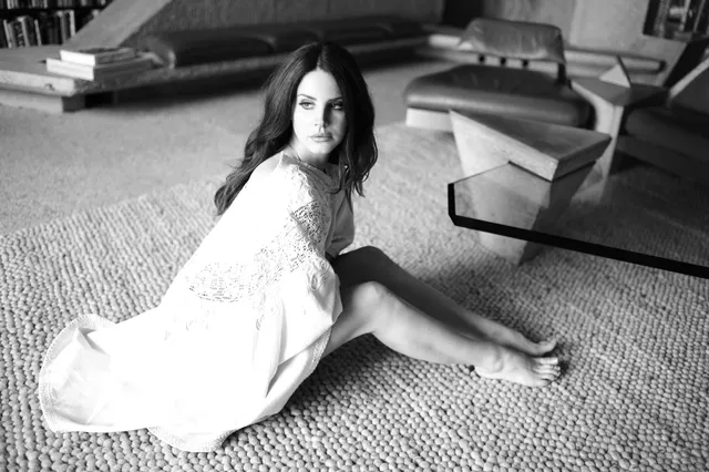 Lana Del Rey sitting barefoot on a carpet in a monochrome portrait.