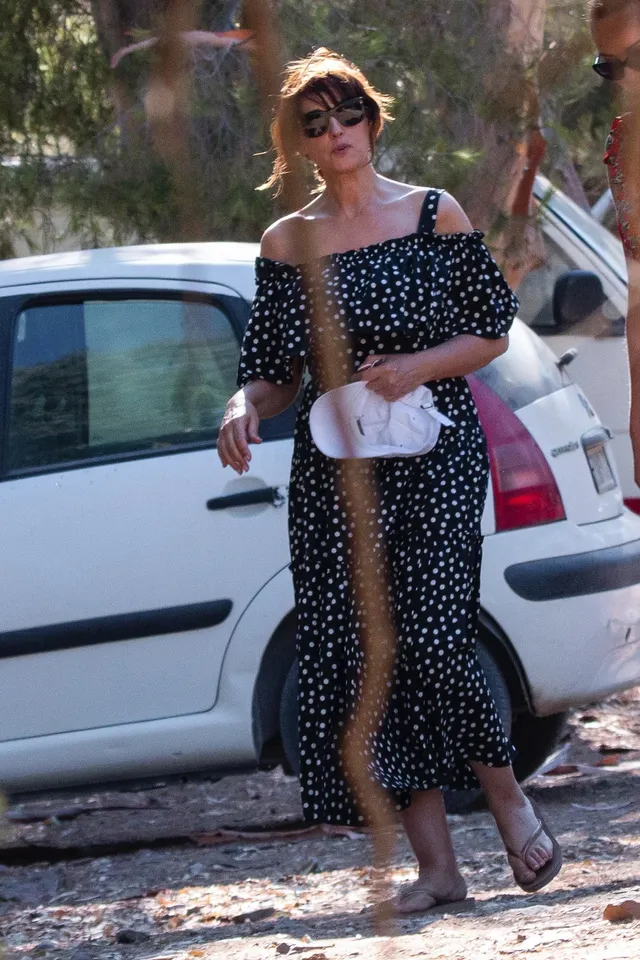 Monica Bellucci walking beside a car in a dotted black dress.