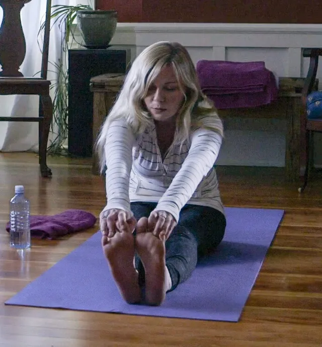 Kirsten Dunst stretching barefoot on a purple exercise mat.