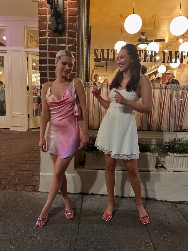 Lola Tung posing with a friend in a pale dress and pink heels.
