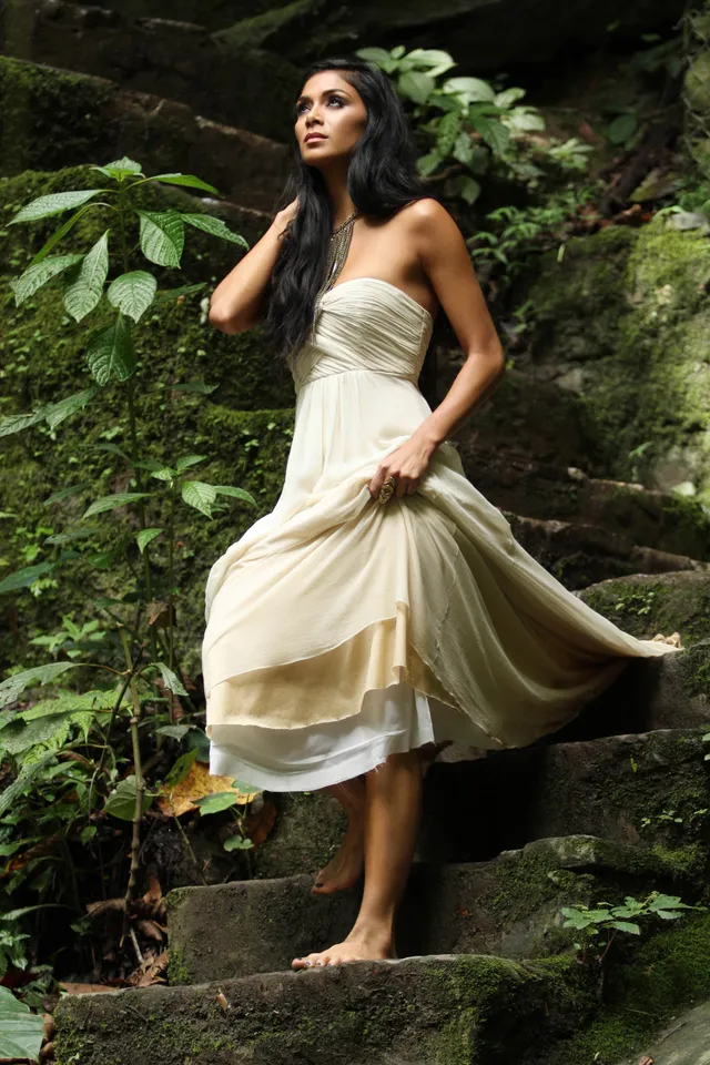 Nicole Scherzinger standing barefoot on stone steps in a pale dress.