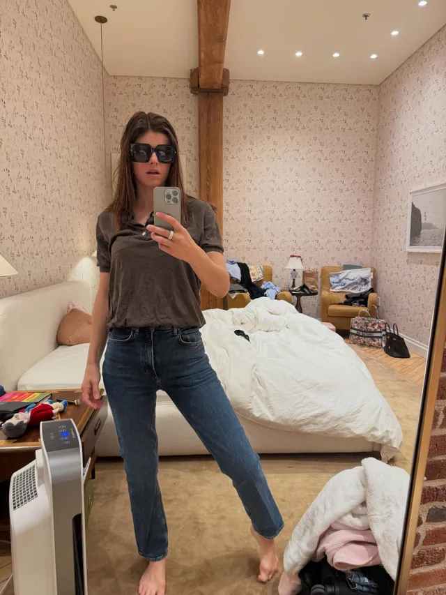 Alexandra Daddario taking a barefoot mirror photo in jeans.