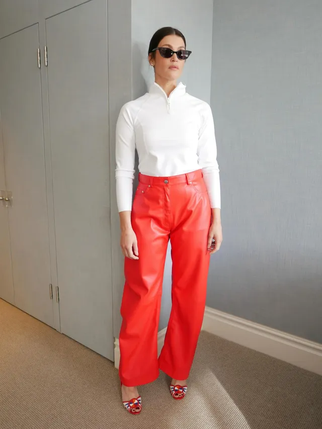 Gemma Arterton posing in a white shirt and red trousers.