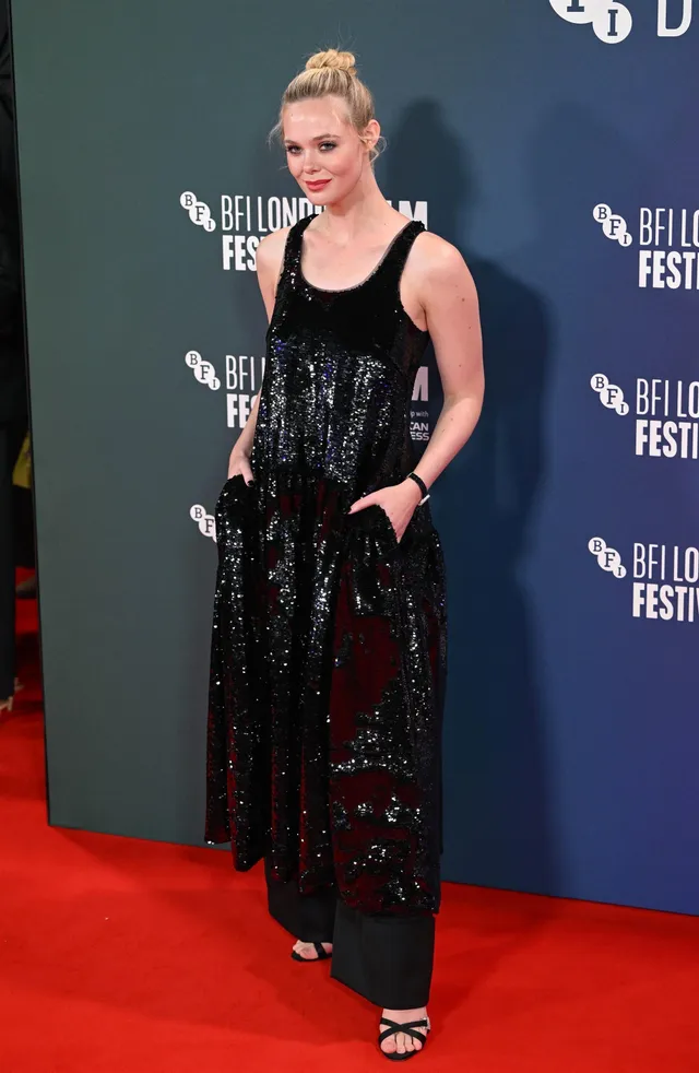 Elle Fanning posing in a black outfit and heels on a red carpet.
