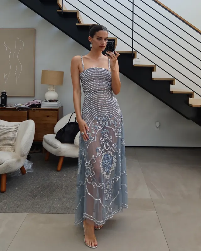 Sara Sampaio standing barefoot in a silver embellished dress for a mirror photograph.