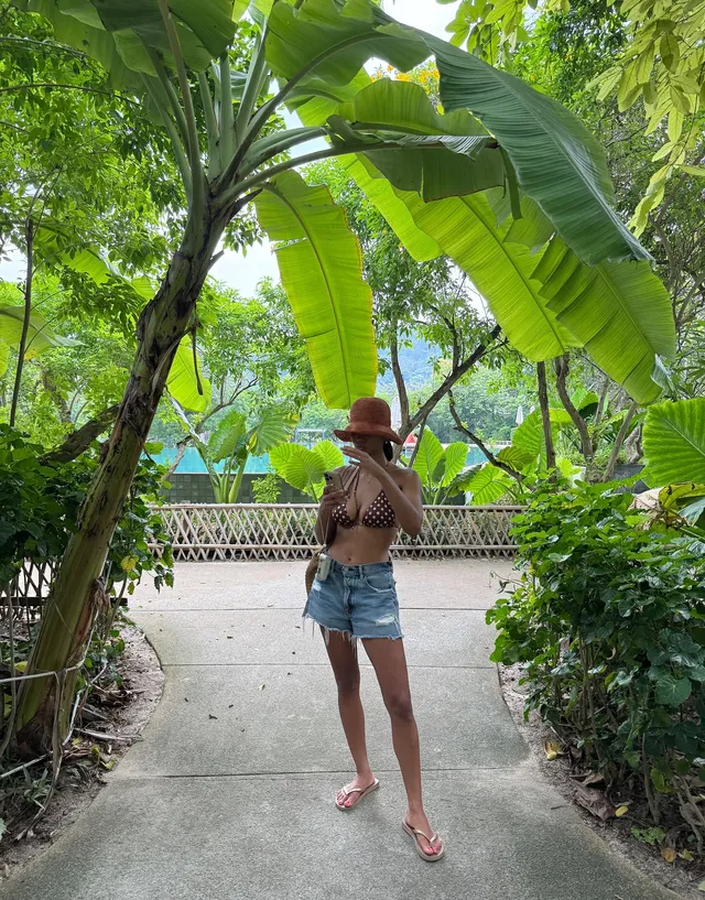 Greta Onieogou standing outdoors in denim shorts, a sun hat and flat sandals.