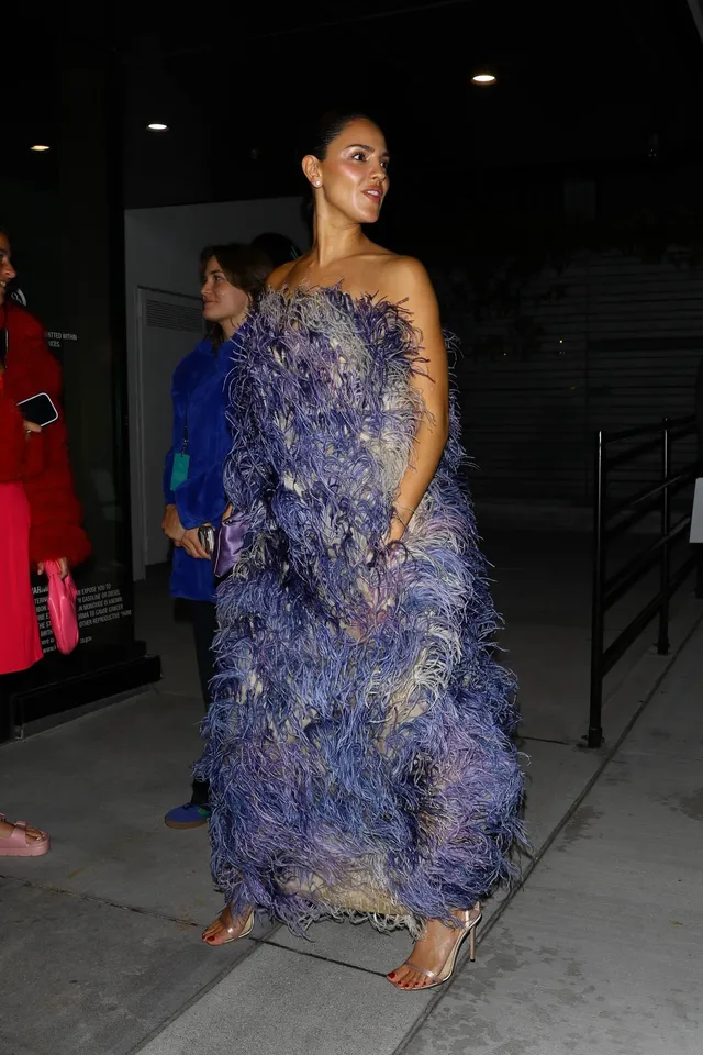 Eiza González wearing a blue feathered gown and heels outdoors.