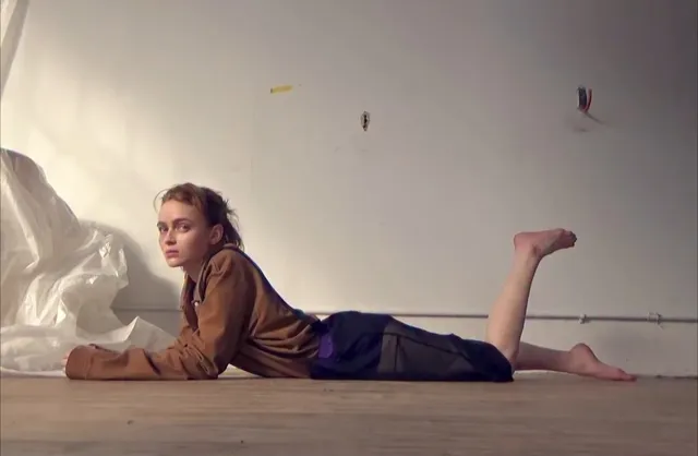 Sadie Sink lying on a floor with a bare foot raised.