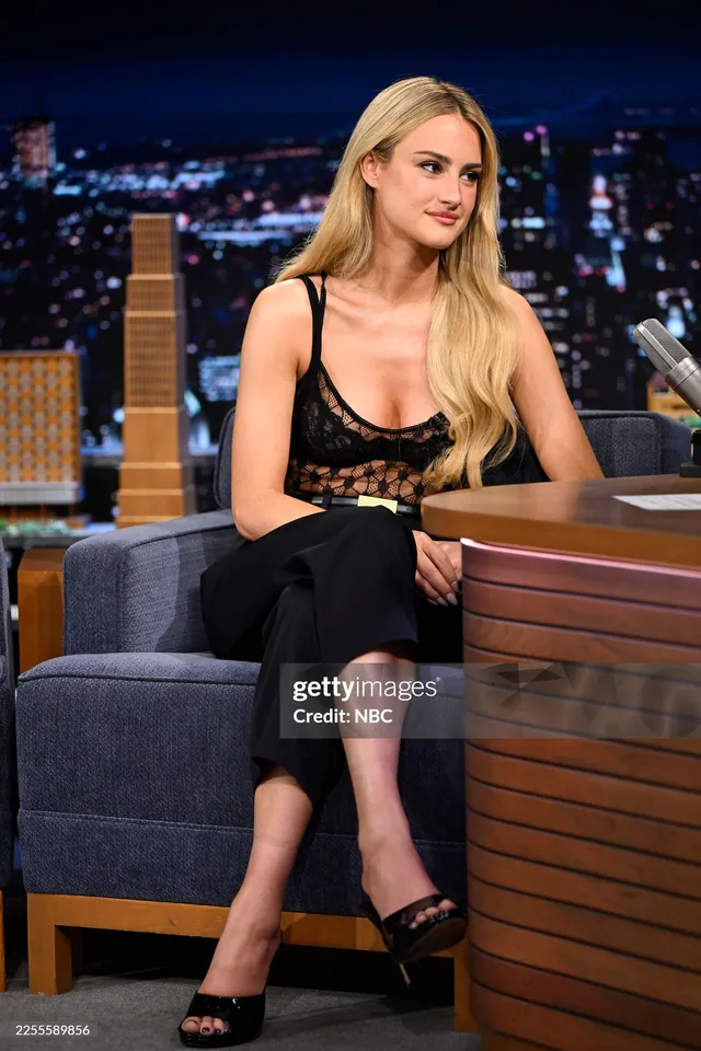 Grace Van Patten sitting on a talk show in a black outfit and heels.