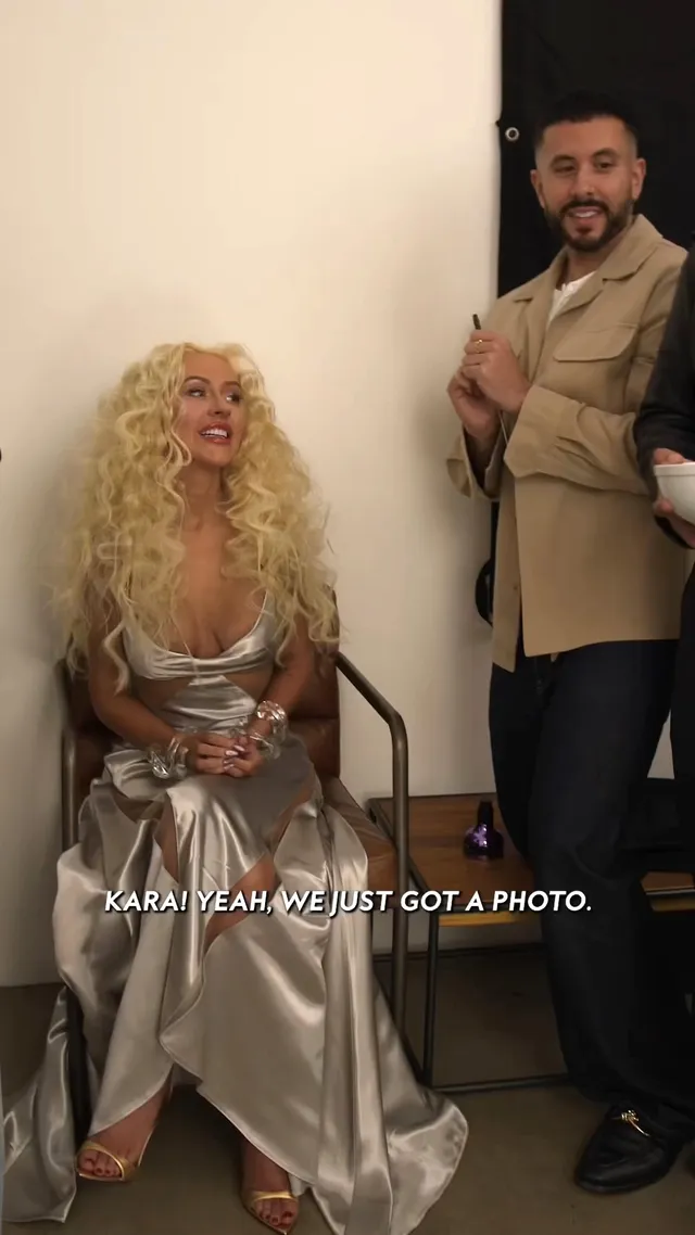 Christina Aguilera sitting in a metallic gown and pale pointed heels.