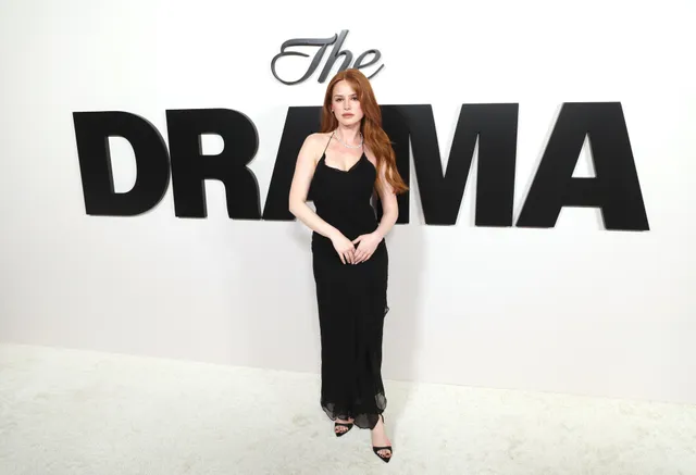 Madelaine Petsch posing at a premiere in a long black dress and heels.