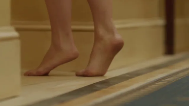 Olivia Wilde standing on tiptoe with bare feet in a film scene.