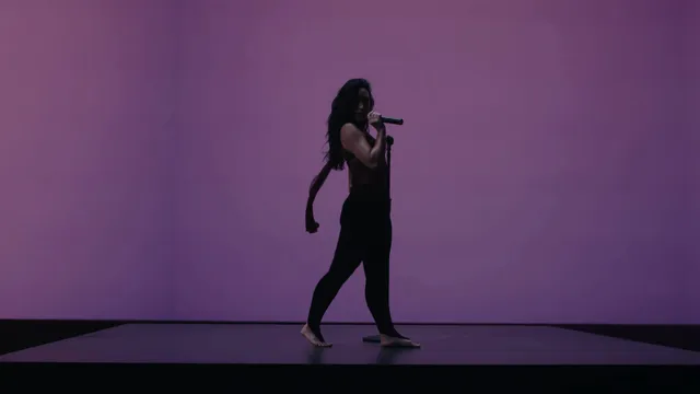 Demi Lovato singing barefoot in a purple-lit studio setting.