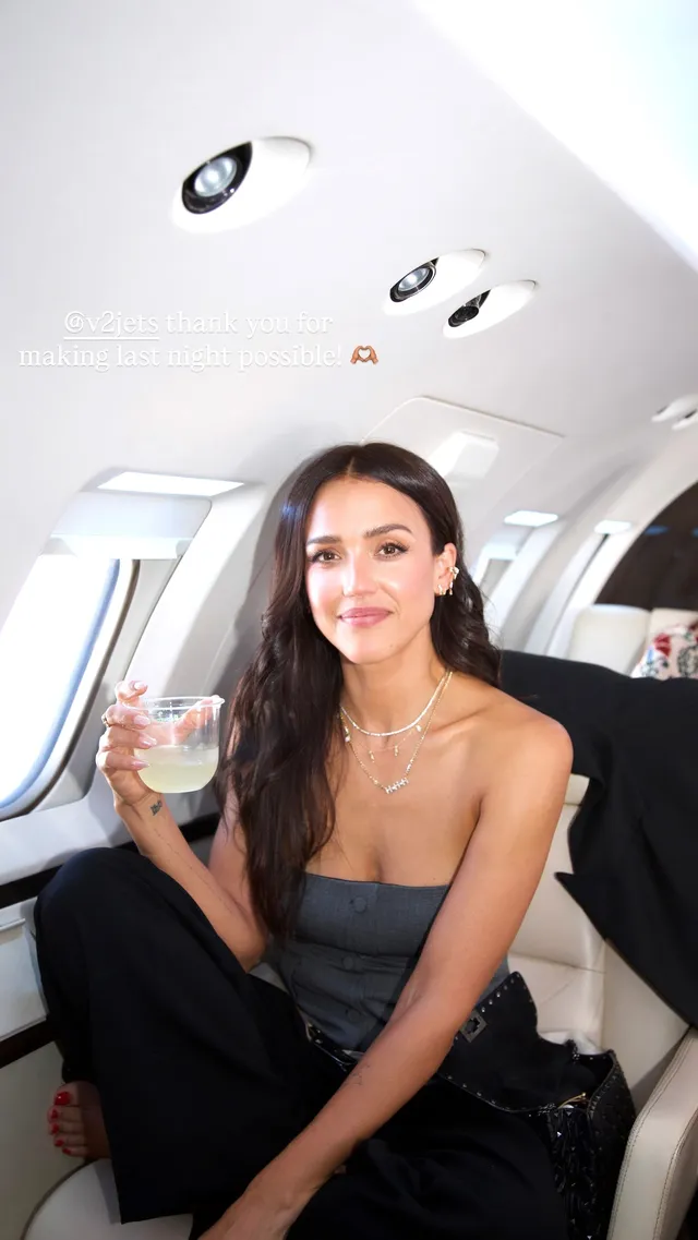 Jessica Alba sitting aboard a plane wearing a black outfit.