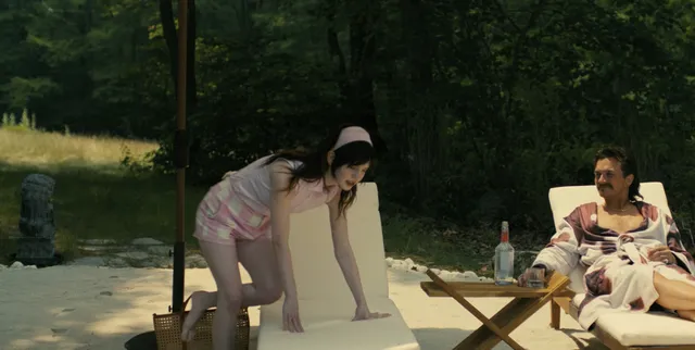 Sophie Thatcher kneeling on a sun lounger beside a man in a film scene.