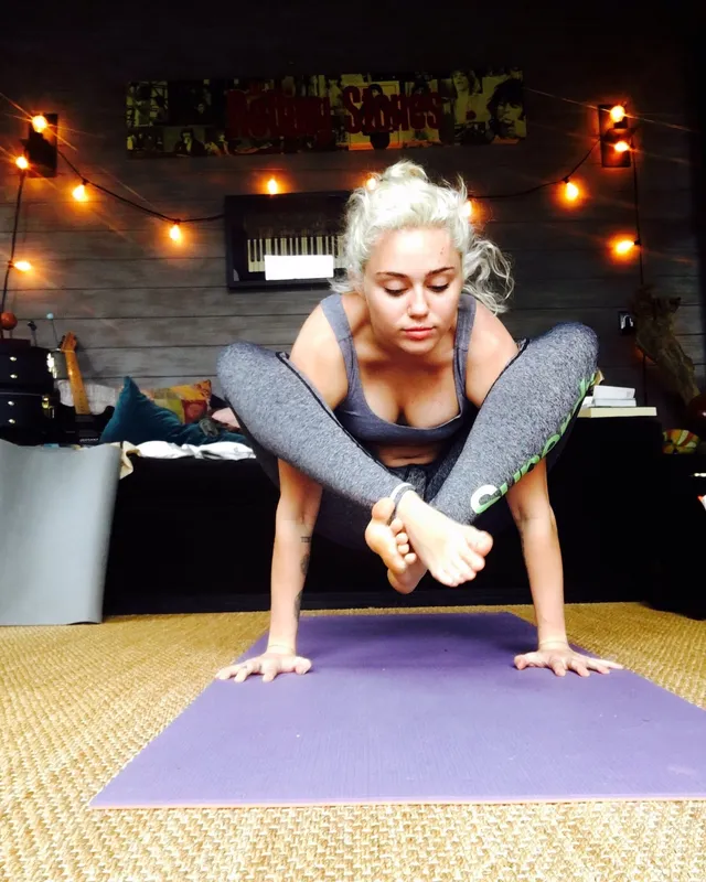 Miley Cyrus balancing barefoot on a yoga mat.