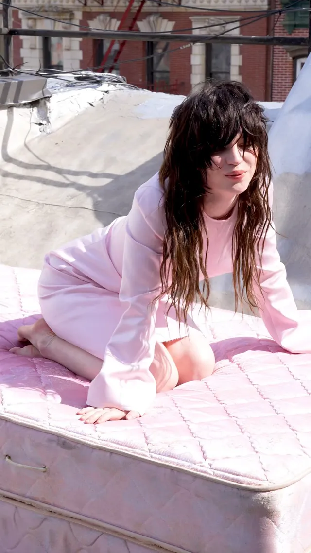 Sophie Thatcher kneeling barefoot on a pink rooftop mattress.