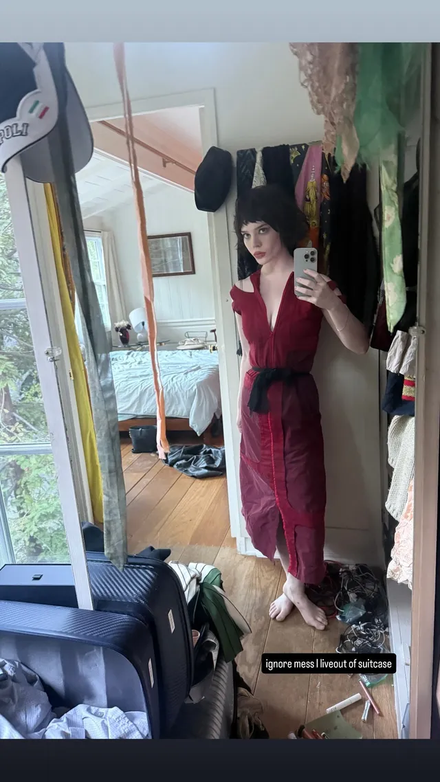 Sophie Thatcher taking a mirror selfie barefoot in a red dress.