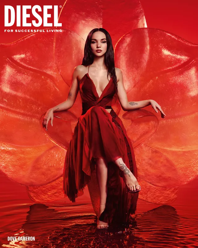 Dove Cameron posing barefoot in a red dress against a red backdrop.