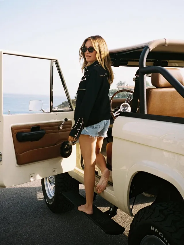 Ashley Tisdale sitting in an open vehicle doorway wearing dark flat sandals.