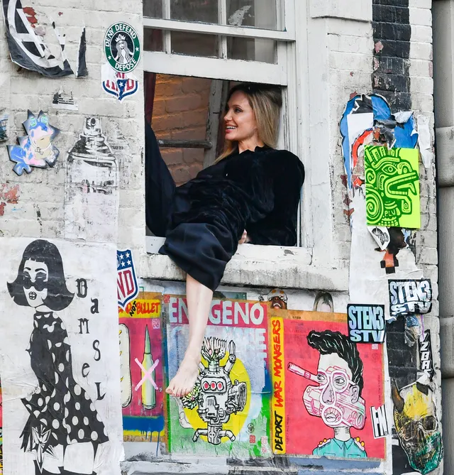 Angelina Jolie a window portrait with bare feet above colourful posters.