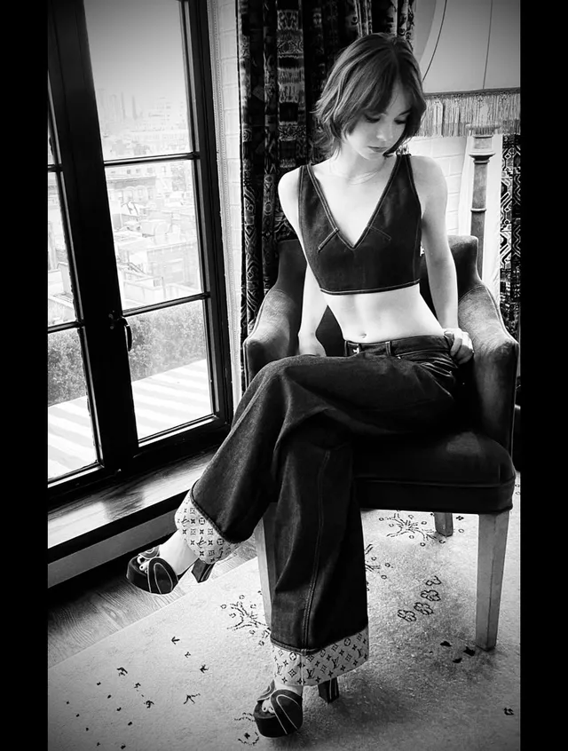 Emma Myers sitting beside a window in patterned socks and sandals.