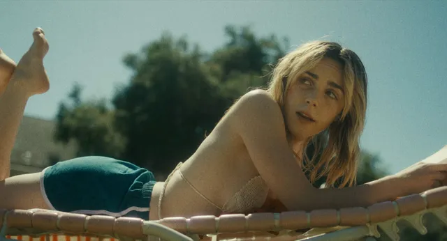 Kiernan Shipka looking up while lying barefoot on a sun lounger.