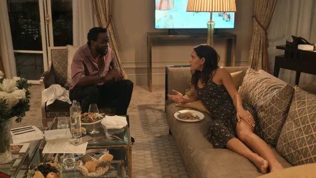 Adria Arjona reclining barefoot on a sofa in a film scene.