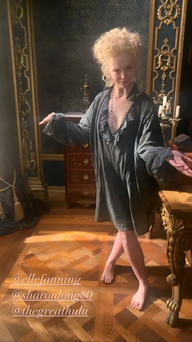 Elle Fanning standing barefoot in a gray robe indoors.