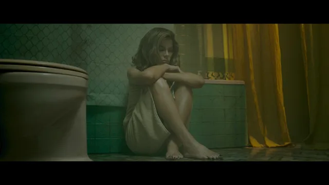 Kate Beckinsale sitting barefoot beside a wall in a screen image.