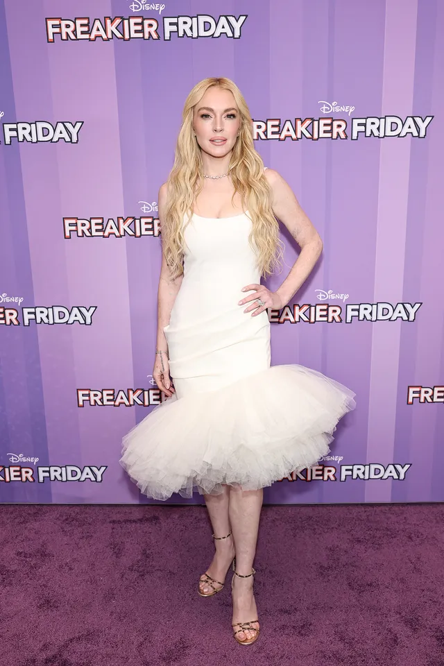 Lindsay Lohan posing in a white dress and heels at a film event.