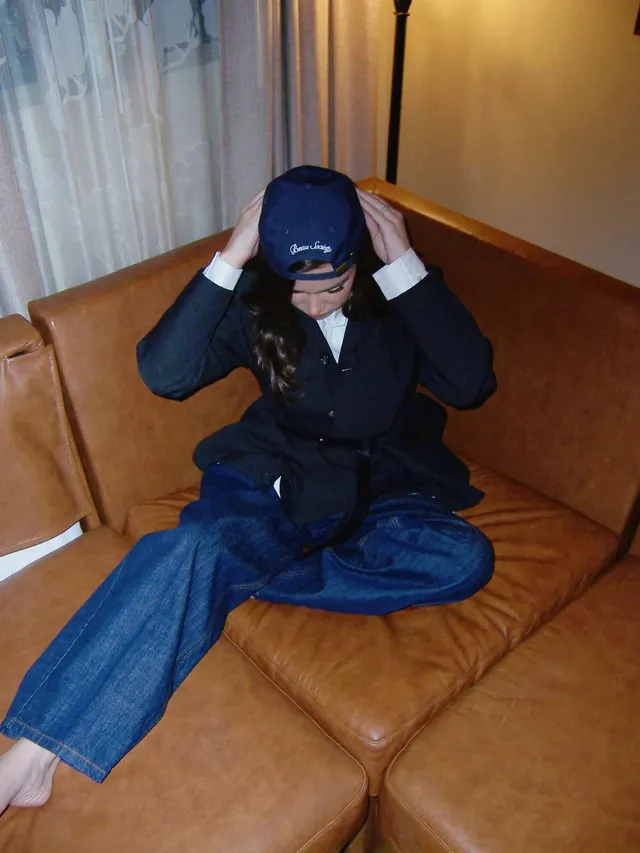 Hailee Steinfeld sitting barefoot on a leather sofa wearing a blue suit.