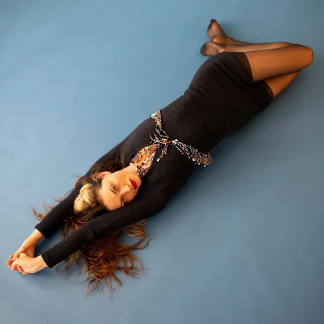 Phoebe Tonkin lying on a studio floor in a black outfit.