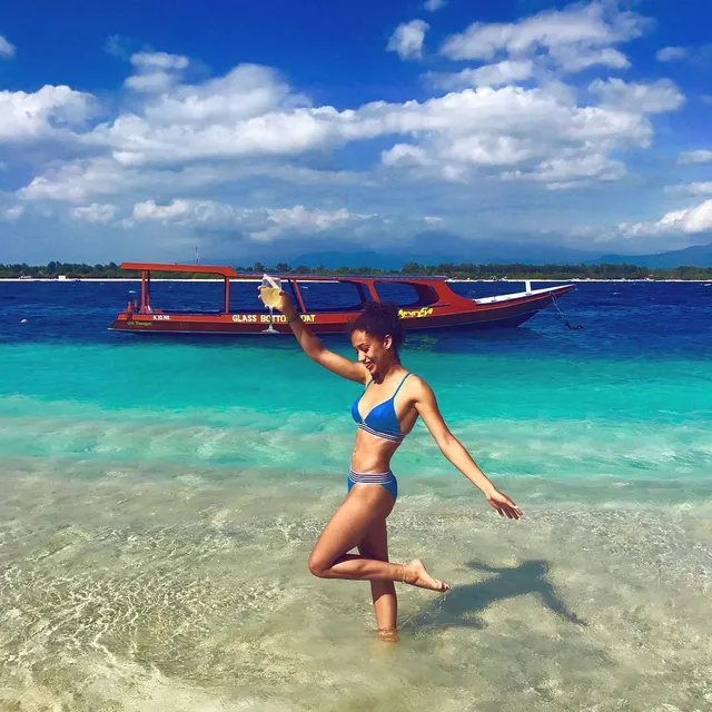 Samantha Logan standing barefoot in shallow sea water in a blue bikini.