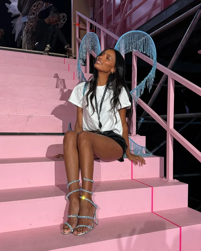 Jasmine Tookes sitting on pink steps in metallic heeled sandals.