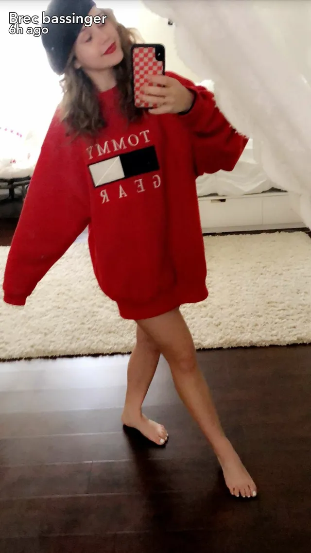 Brec Bassinger taking a mirror selfie barefoot in a red sweatshirt.