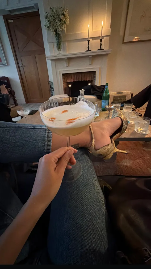 Emily Ratajkowski resting a heel beside a drinks table indoors.