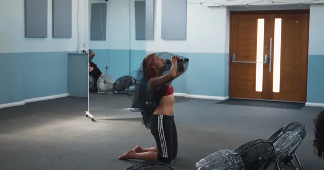 Naomi Scott kneeling barefoot beside fans in a rehearsal room.