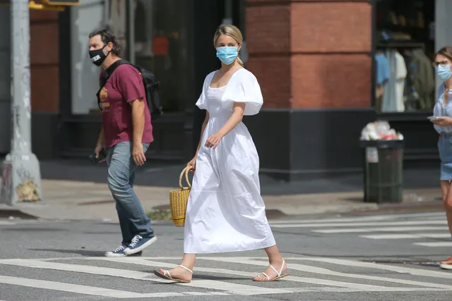 Dianna Agron walking outdoors in a white dress and flat sandals.