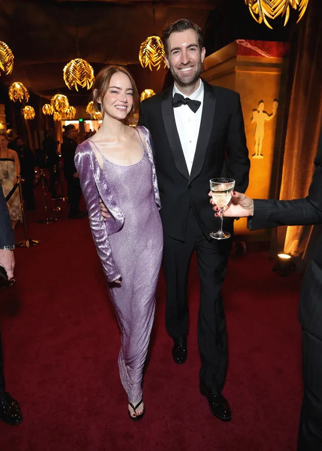 Emma Stone standing with an award in a lavender dress and pointed heels.
