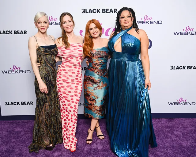 Isla Fisher posing with cast members on a purple carpet.