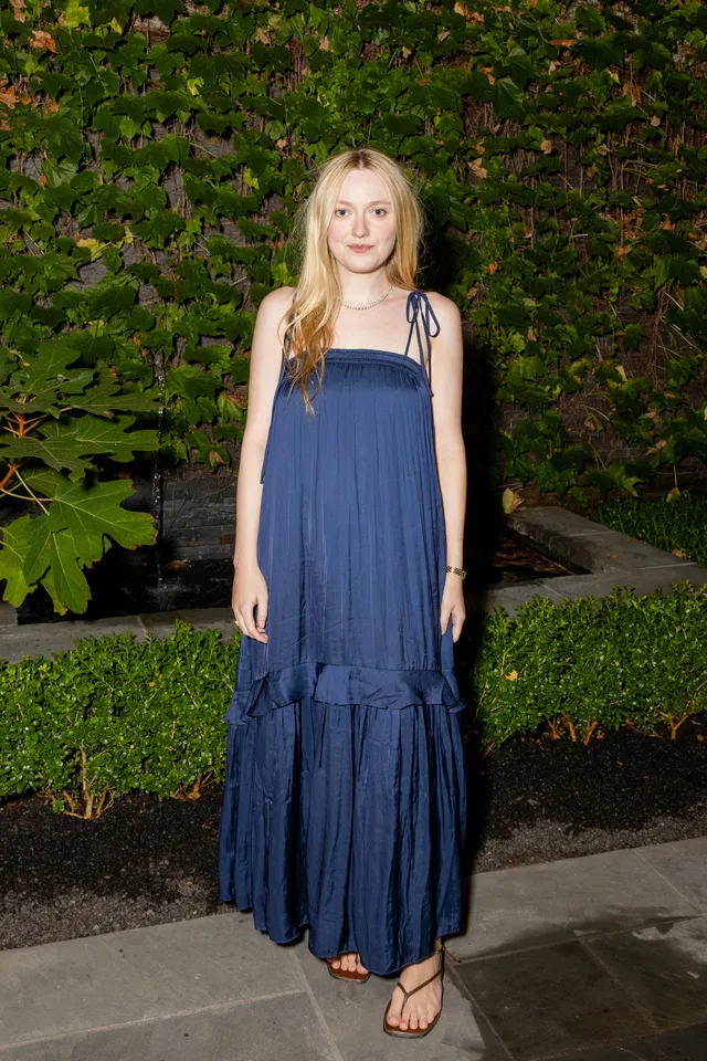 Dakota Fanning posing in a blue dress and sandals outdoors.